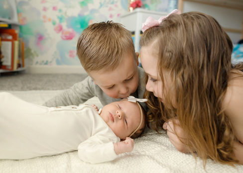 young boy and girl kiss their infant sister as she sleeps on the floor