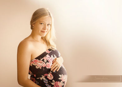 pregnant blonde woman holds her belly in a floral dress in Omaha, ne