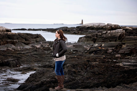 woman looks over rocks in front of lighthouse in New Hampshire ocean front