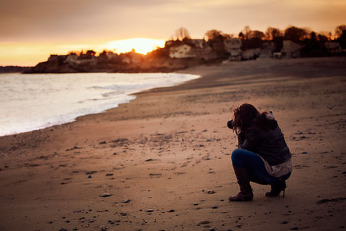 woman kneels to take picture of beach front properties in Maine