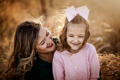 Mother smiles as daughter laughs in sunlit field during fall family photos in Gretna, NE