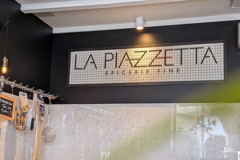 Enseigne La Piazzetta Épicerie Fine sur un mur noir.