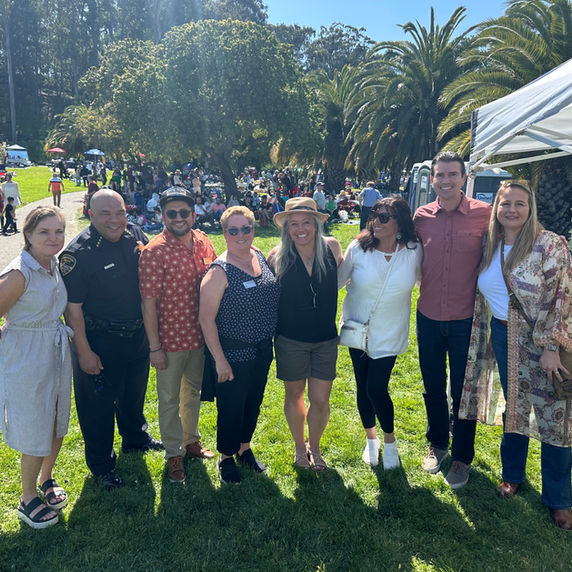 Group of people smiling together at a sunny outdoor park event.