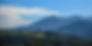 Lush green hills with a large blue mountain under a bright sky.