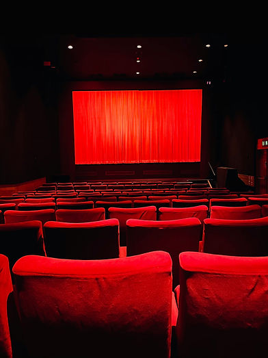Une salle de spectacle déserte. les fauteuils et le rideau de la scène sont rouge écarlate