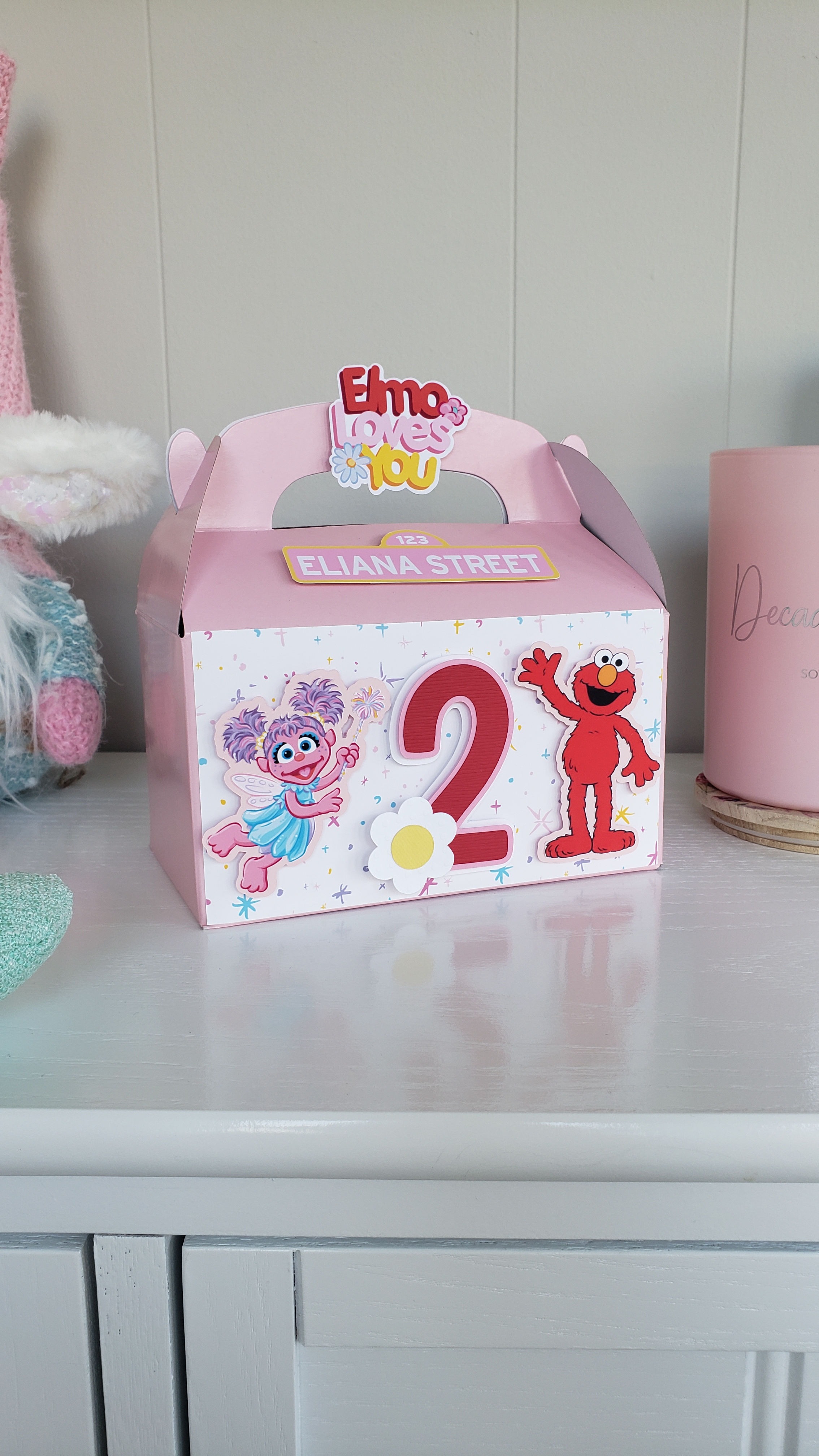 Pink favor box with image of Abby Cadabby and Elmo from Sesame Street, daisies and a number 2.