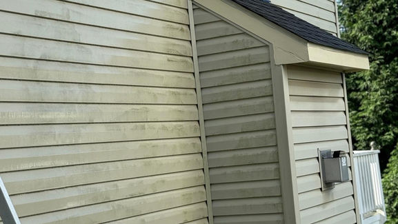 Person using a power washer on a home exterior to remove dirt and grime.