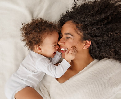 A mother and baby close together. The mother is smiling as the baby touches her face.