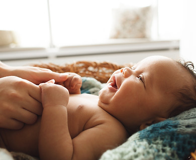 Baby smiling at mother, close-up. Adorable newborn child looking up at mother and holding