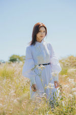 Emi in a light blue dress standing in a field of tall grass.
