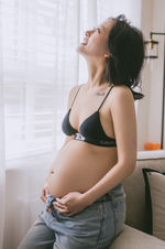 Letitia smiling and holding her pregnant belly by a window