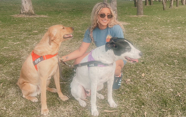A smiling woman sitting with her two dogs in a peaceful park setting, radiating love and connection.