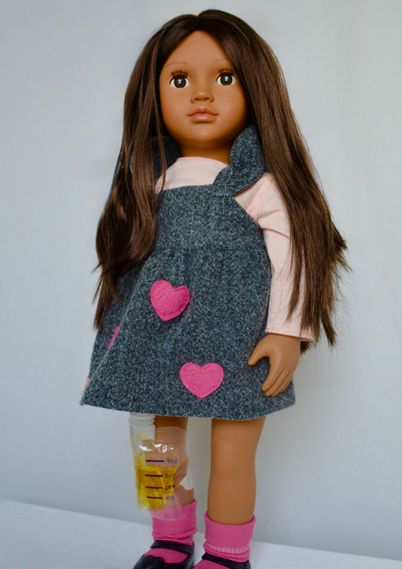 A hispanic girl doll wearing a dress, with a urinary collection bag attached to leg