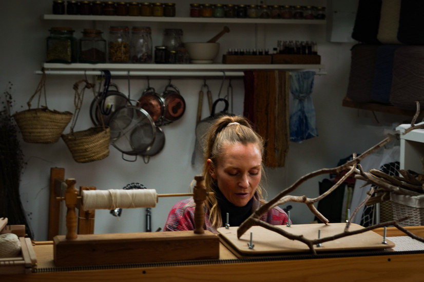 Young woman sitting in her creative studio, looking down at her work which is hidden behind a shelf