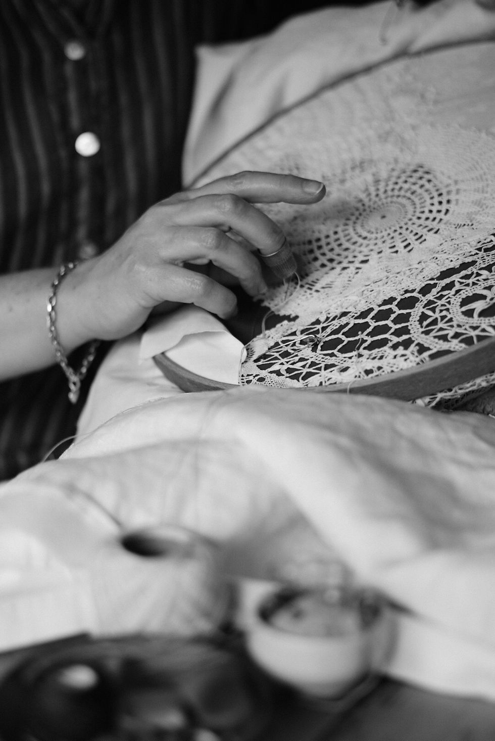 Black and white image of a white woman's hand, quilting in a hoop.