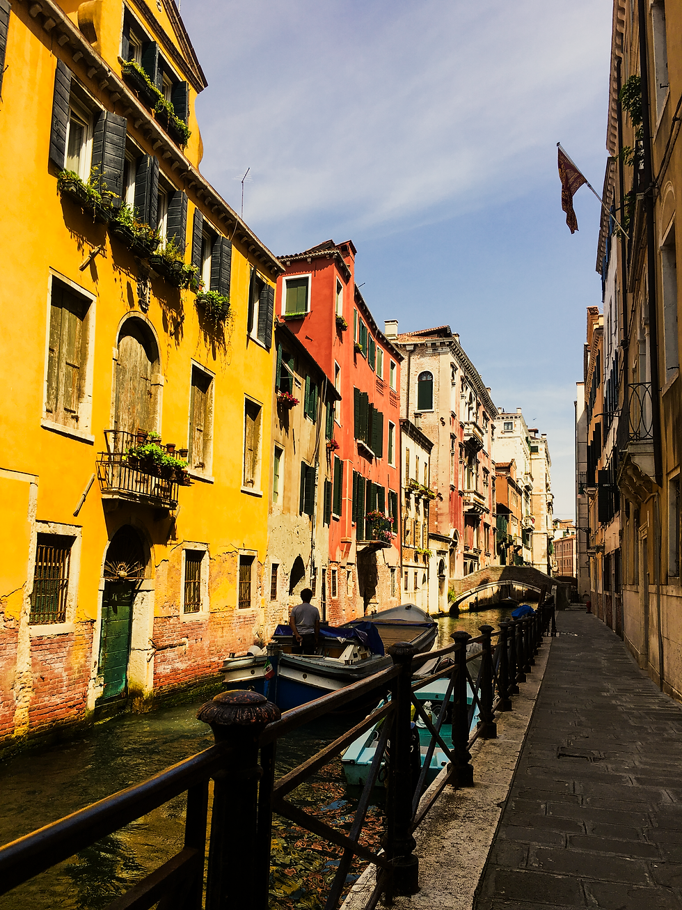 A residential canal in afternoon light, ochre and red facades stepping back along a paved fondamenta, small boats moored at the waterline.