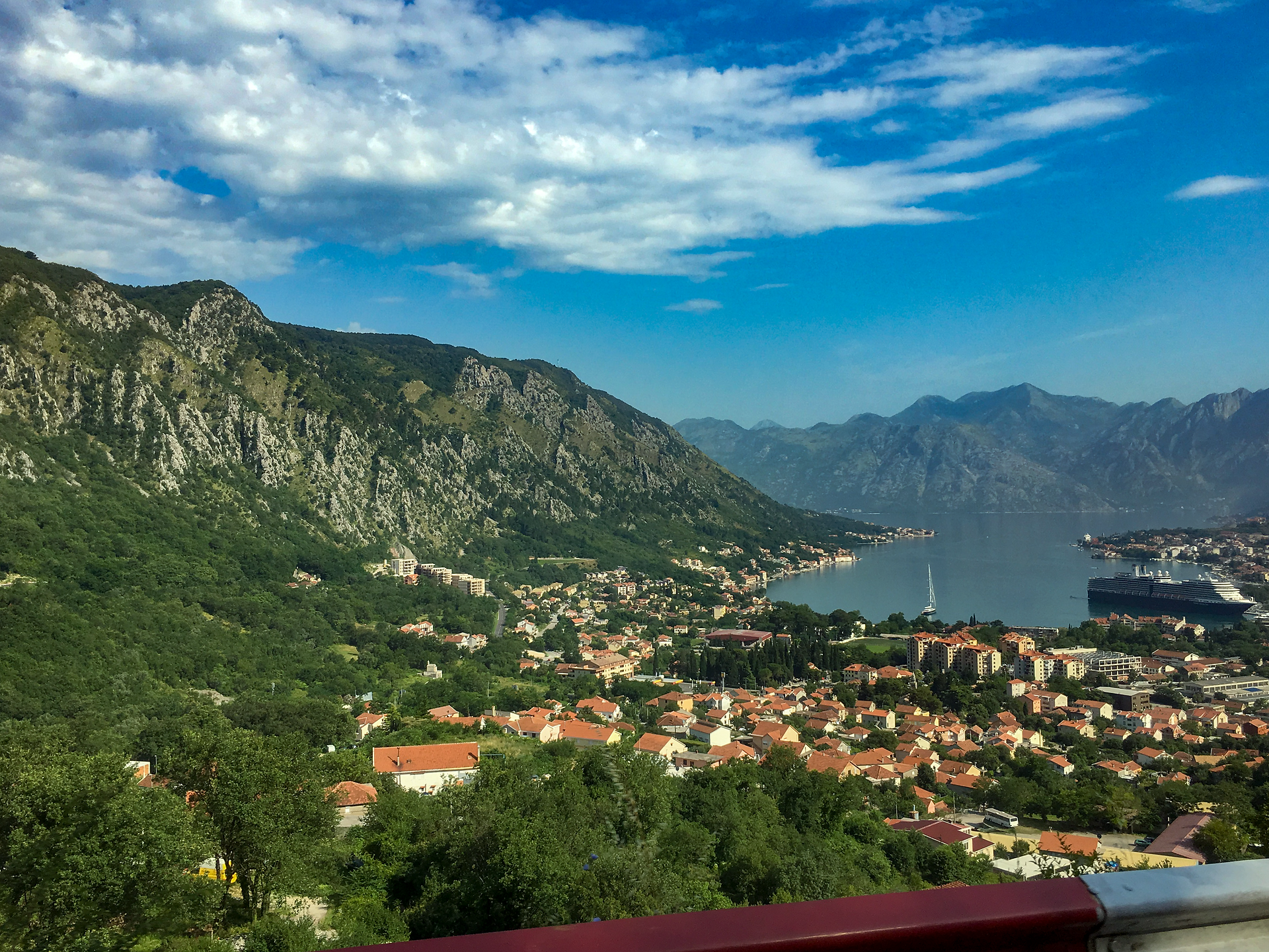Kotor's red roofs and a docked cruise ship far below the serpentine road, with the bay and mountains beyond