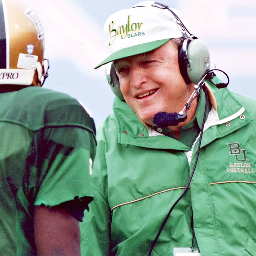 Coach Grant Teaff on the Baylor sidelines in headset and green jacket during a game.