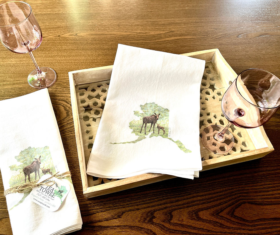 Tea towel with moose and calf design on the front sitting on a wooden tray with purple wine glasses