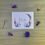 Thumbnail: a thank you card with pink and purple flowers on the front sits on a table with small flower blossoms sitting around it