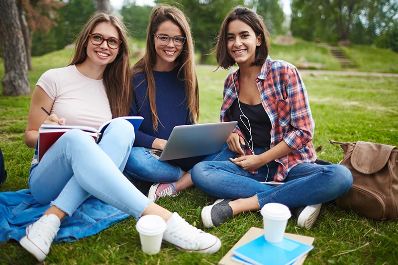 a group of women sitting on the grass with a laptop