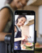 Woman cooking with a cellphone; recording and smiling. Content Creation; Brummble Digital