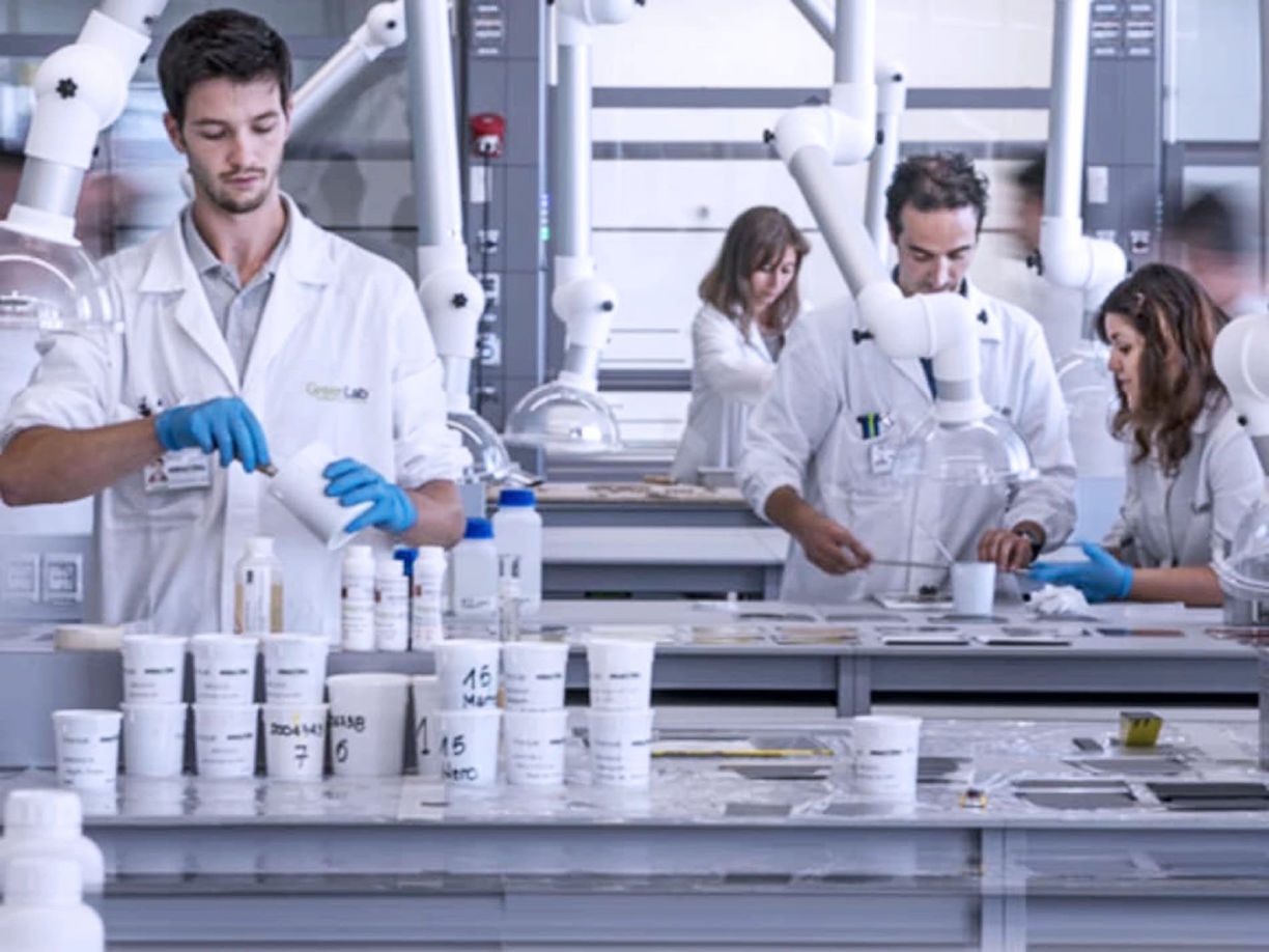 Scientists in lab coats working with beakers, bottles, and equipment in a laboratory.