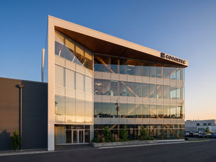 Modern multi-storey glass commercial building at dusk with glazed entry doors at street level