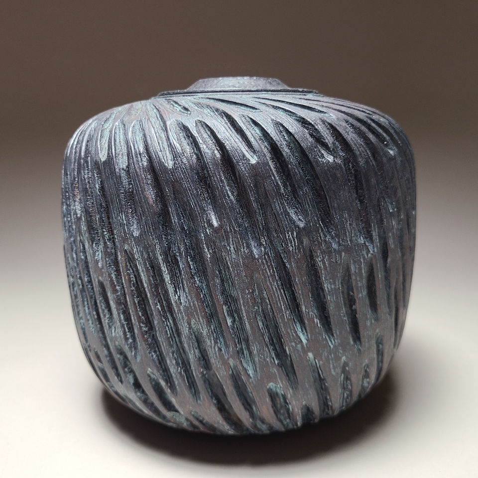 Textured wood vessel titled ‘Survivor #2’ by Roberto Ferrer, turned and carved in maple with a dark metallic finish resembling aged, corroded metal from an archaeological site