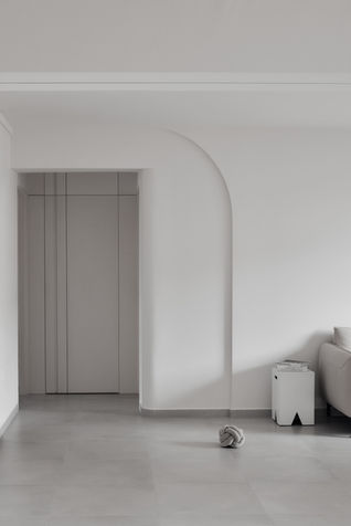 This minimalist living room design in a 4-room resale flat in Bishan features a concealed bomb shelter door seamlessly integrated into the wall. The space is accentuated by a curved indent, adding a soft architectural detail that complements the modern, clean aesthetic. The neutral tones and smooth surfaces highlight the understated elegance of this HDB home, designed by Comfort Home Interior.