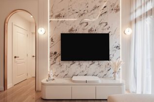 Close-up view of the luxurious TV wall feature in a modern luxe condo designed by Comfort Home Interior. The wall is clad in stunning marble tiles with intricate veining that adds depth and texture, flanked by vertical fluted panels that create a refined and sophisticated look. A sleek, minimalist TV console sits below, continuing the marble pattern for a cohesive design. The arched doorway and soft, ambient lighting fixtures add a touch of warmth and elegance to the space, making this wall feature a true centerpiece of the living area, blending classic luxury with modern design sensibilities.