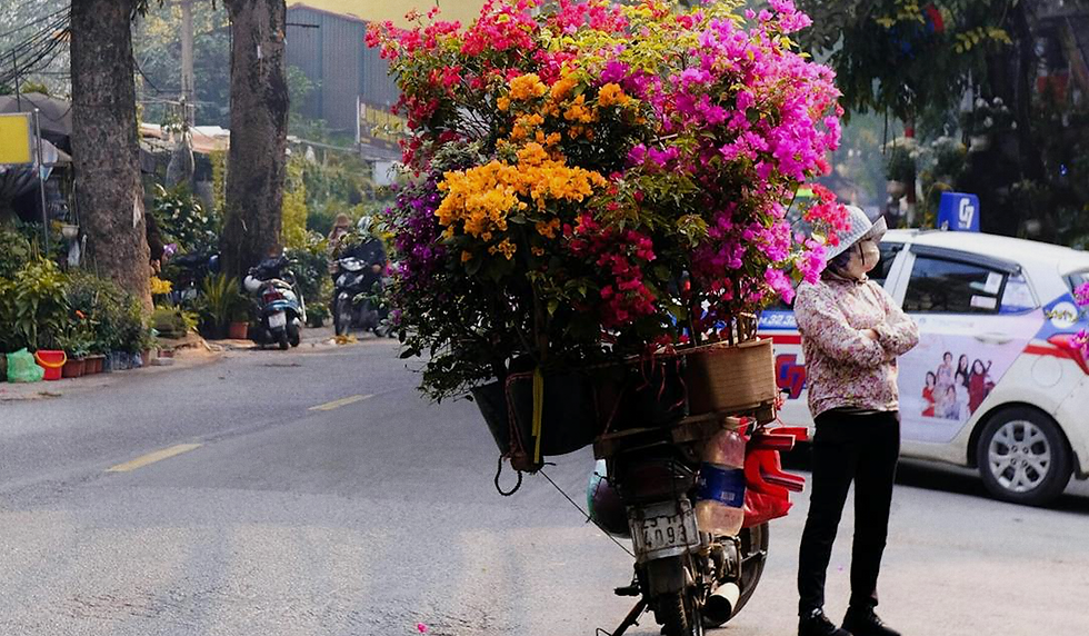 una moto che trasporta fiori di ogni colore e una donna affianco in piedi con le braccia incrociate