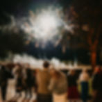 Couple watches fireworks with crowd at night at blank canvas wedding venue in Fife. Woman wears a denim jacket with "Bride" written on it. Trees and smoke in the background.