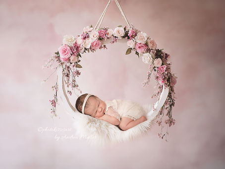 Ein neugeborenes Baby liegt in einer mit Blumen geschmückten Schaukel während eines Neugeborenen-Shooting in Langenfeld. Das Bild ist ein Artwork-Motiv der Fotografin Andrea Müller bei photokissesart in Langenfeld