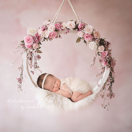 Ein neugeborenes Baby liegt in einer mit Blumen geschmückten Schaukel während eines Neugeborenen-Shooting in Langenfeld. Das Bild ist ein Artwork-Motiv der Fotografin Andrea Müller bei photokissesart in Langenfeld