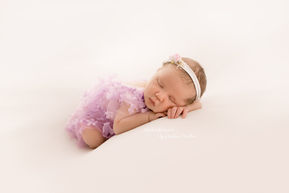 Ein Neugeborenes Mädchen wurde von der auf Babys spezialisierten Fotografin Andrea Müller in Langenfeld fotografiert. Das Baby trägt einen fliederfarbenen Romper, der mit Blümchen verziert ist. Das Fotostudio photokissesart stellt alle Materialien bereit.