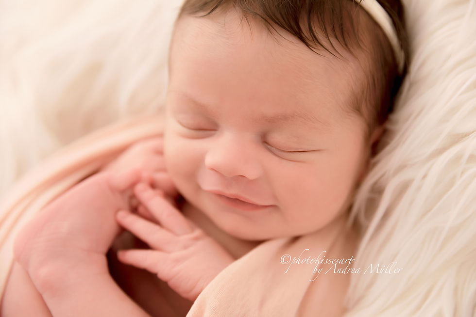 Schlafendes Baby in rosa Decke, liegend auf weißem, flauschigem Hintergrund, lächelt sanft. Das Foto entstand bei einem Newborn-Shooting in Langenfeld bei photokissesart-Andrea Müller Fotografie. Das Fotostudio liegt an der Grenze zu Leverkusen, Monheim und Düsseldorf