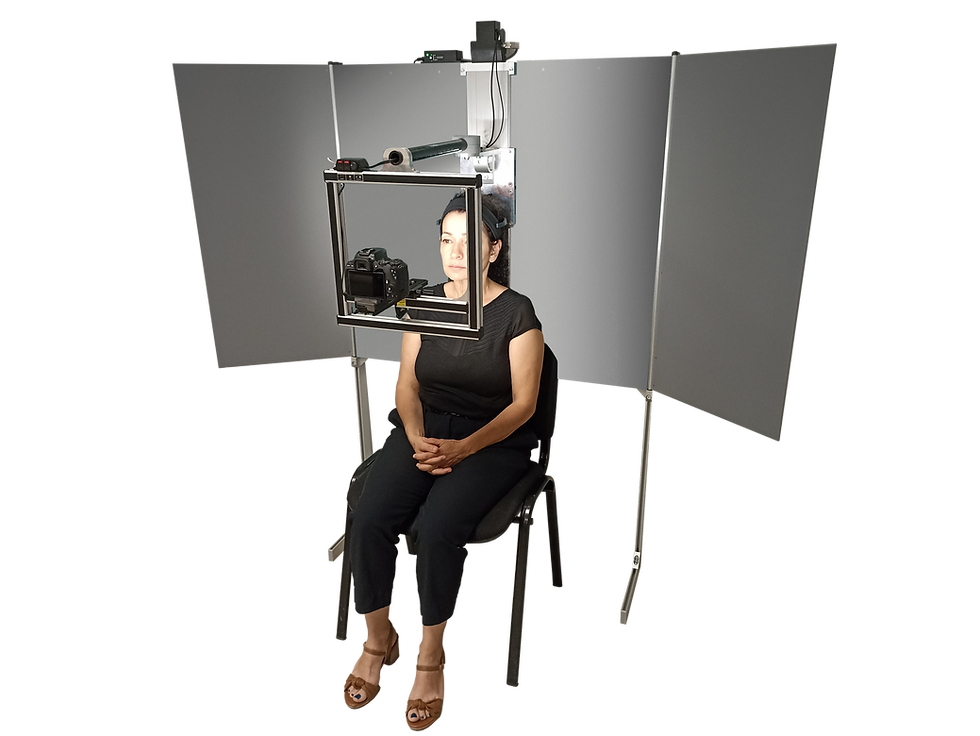 A woman sits in a chair facing a mounted camera setup with gray panels. She appears calm in a neutral, indoor setting.