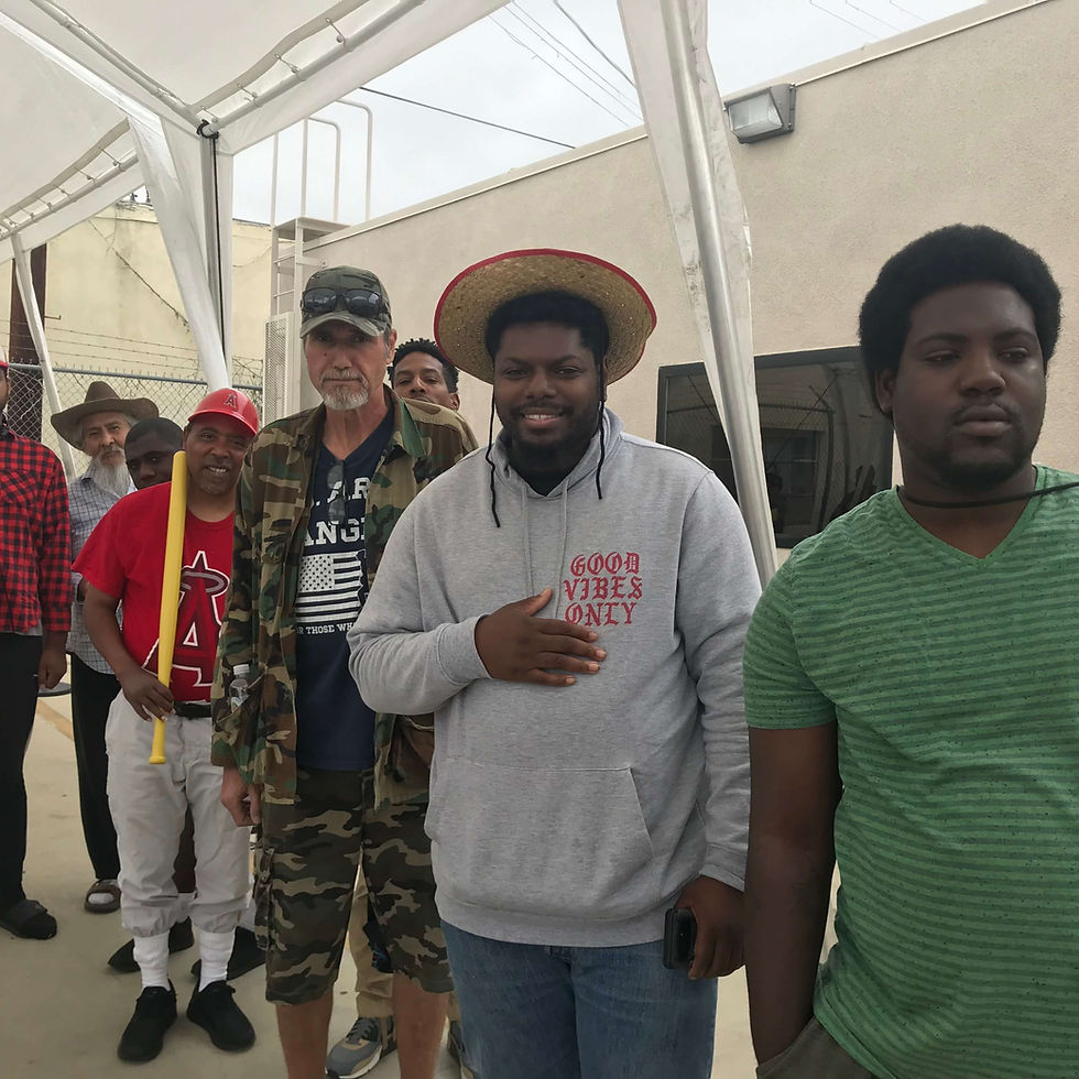 A group of men stands together outdoors under a canopy, some smiling and wearing casual attire.