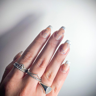 Unghie con french a base nude, decorazioni con cuori vuoti grigi e applicazioni glitter sparsi