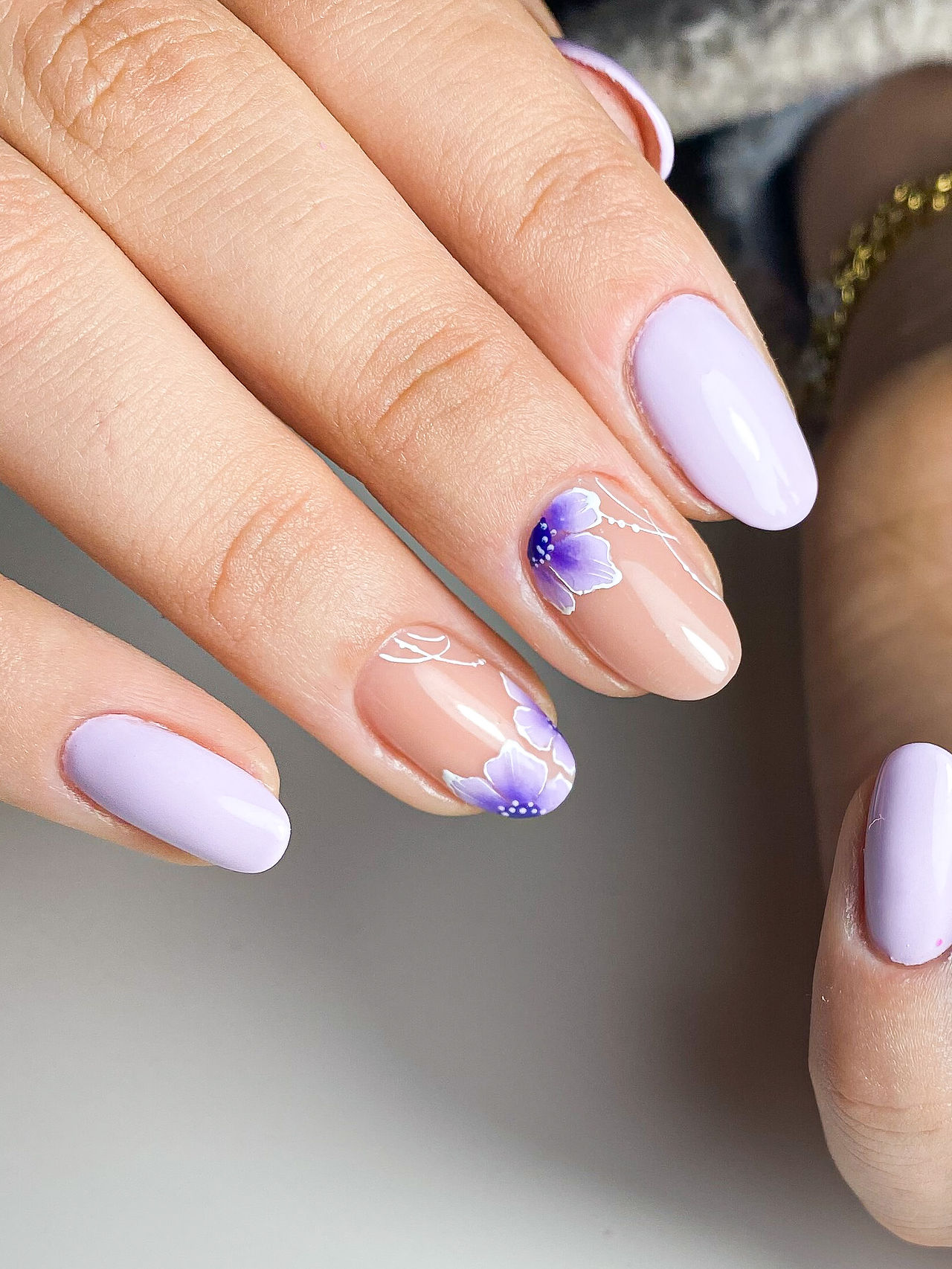 Nail art lilla con fiori viola su base nude. I fiori sono realizzati in stile realistico e gradienti dal viola al lilla