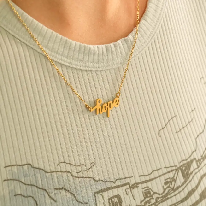 Gold 'hope' necklace on light blue ribbed shirt