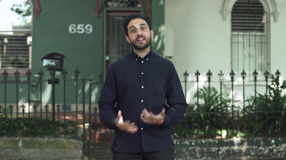 A man in a corporate shirt presenting in front of a terrace house.