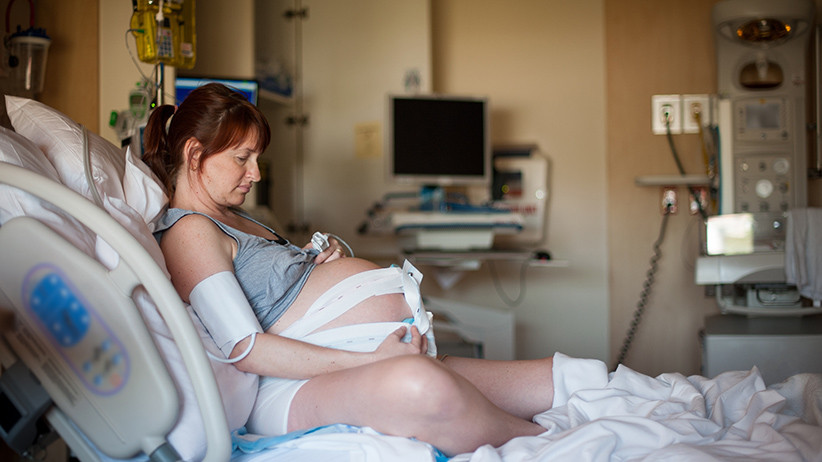 A pregnant woman sits in bed in a hospital birth center during her natural child birth laboring process. She is wearing a fetal monitor to check the vital signs of the baby. She has been laboring for about six hours, but the baby will not be delivered for another 20 hours. (Daniel MacDonald/Getty Images)