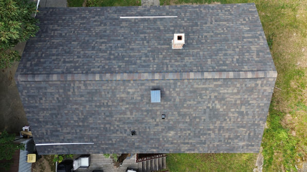 Top-down drone view showing new architectural shingles, chimney, ridge line, and solar attic fan on a Winchendon, MA home.