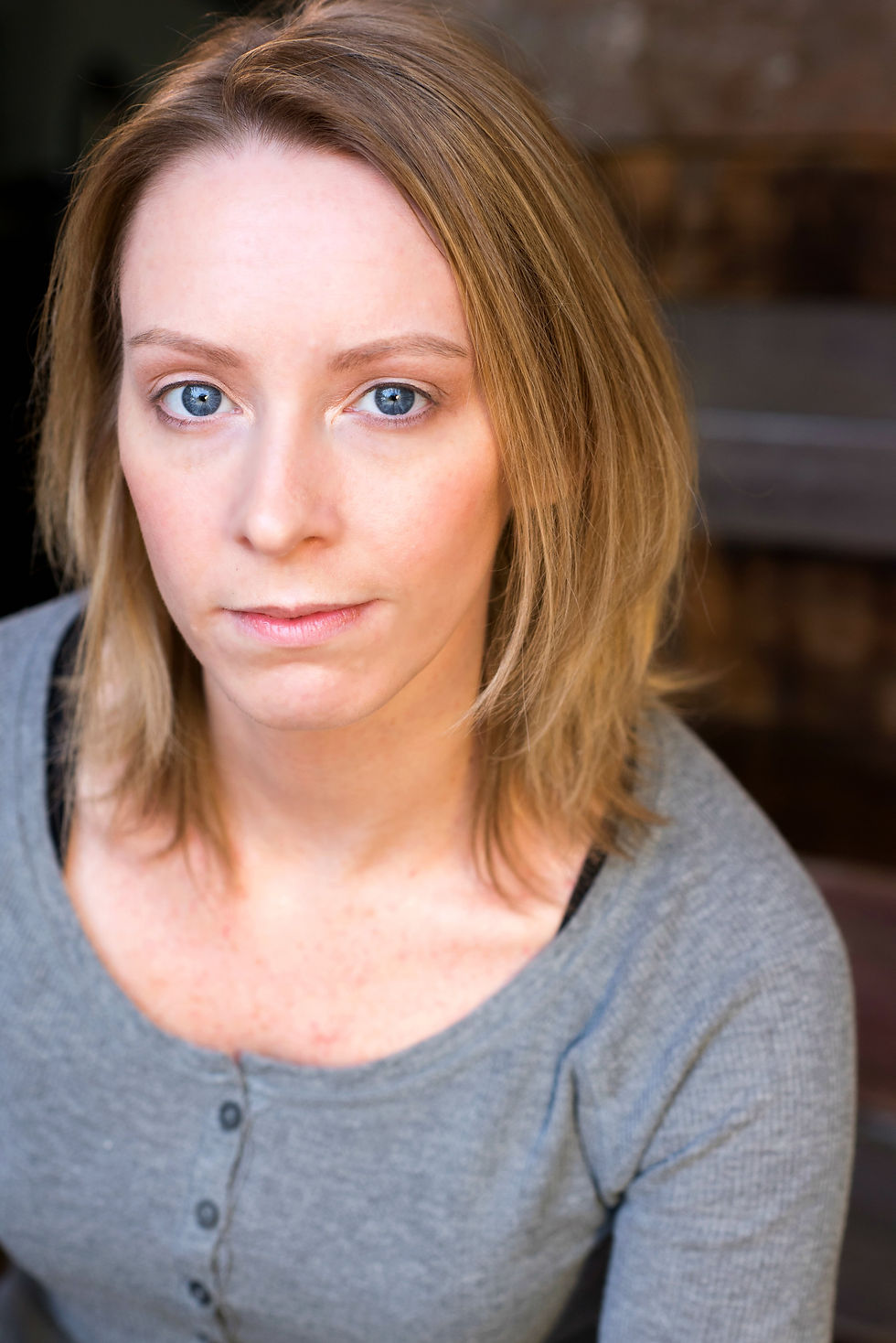A blonde girl with piercing blue eyes wearing a gray shirt looks into the camera.