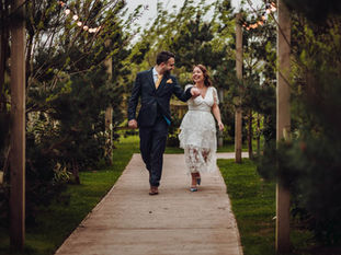 Bride and groom walking hand-in-hand, smiling and laughing at Coton House Farm wedding venue, surrounded by greenery and festoon lights.