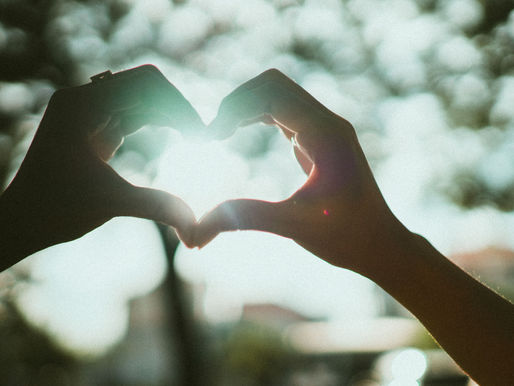 Close-up of hands creating a heart shape under bright sunlight, symbolizing love and connection.