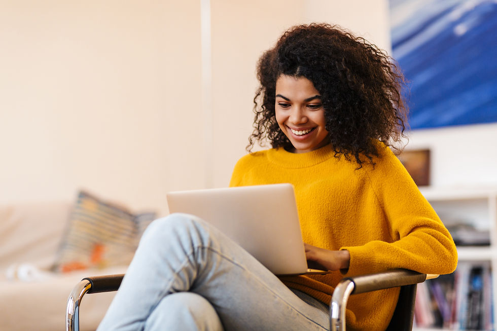 Image of cheerful african american woman using laptop while sitting on chair in living roo