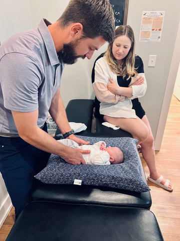 Chiropractor adjusting infant while mom watches